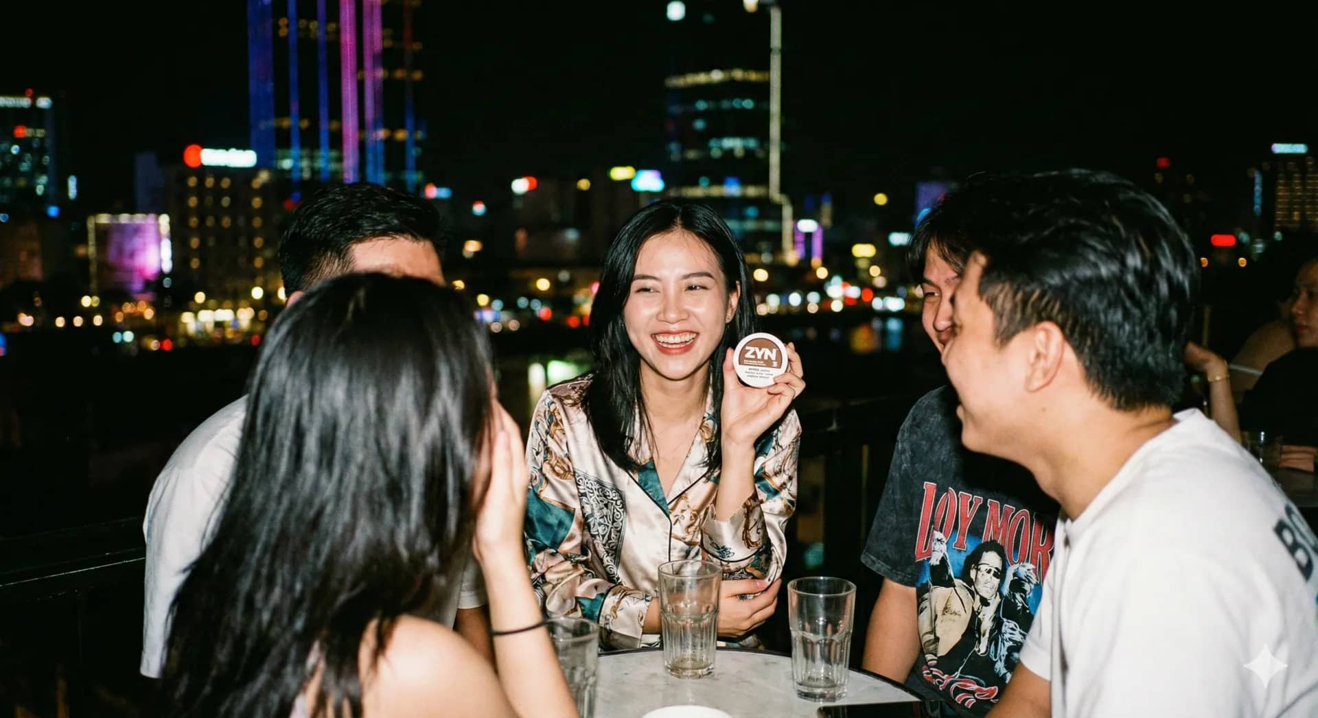 Nhóm bạn bên bàn rooftop ở TP. Hồ Chí Minh, một người cầm hộp ZYN